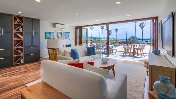 A modern living room with a large window, a sofa, a coffee table, and a dining area with chairs. - Ocean Front * 2 Panoramic Water View Decks * A/C (San Diego)