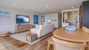 A modern living room with a white sofa, wooden dining table, and a kitchen area visible through an open doorway. - Ocean Front * 3 Water View Patios * A/C (San Diego)