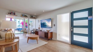 A modern living room with a wooden floor, a round coffee table, a sofa, a TV, and a bookshelf. - Ocean Front * 3 Water View Patios * A/C (San Diego)