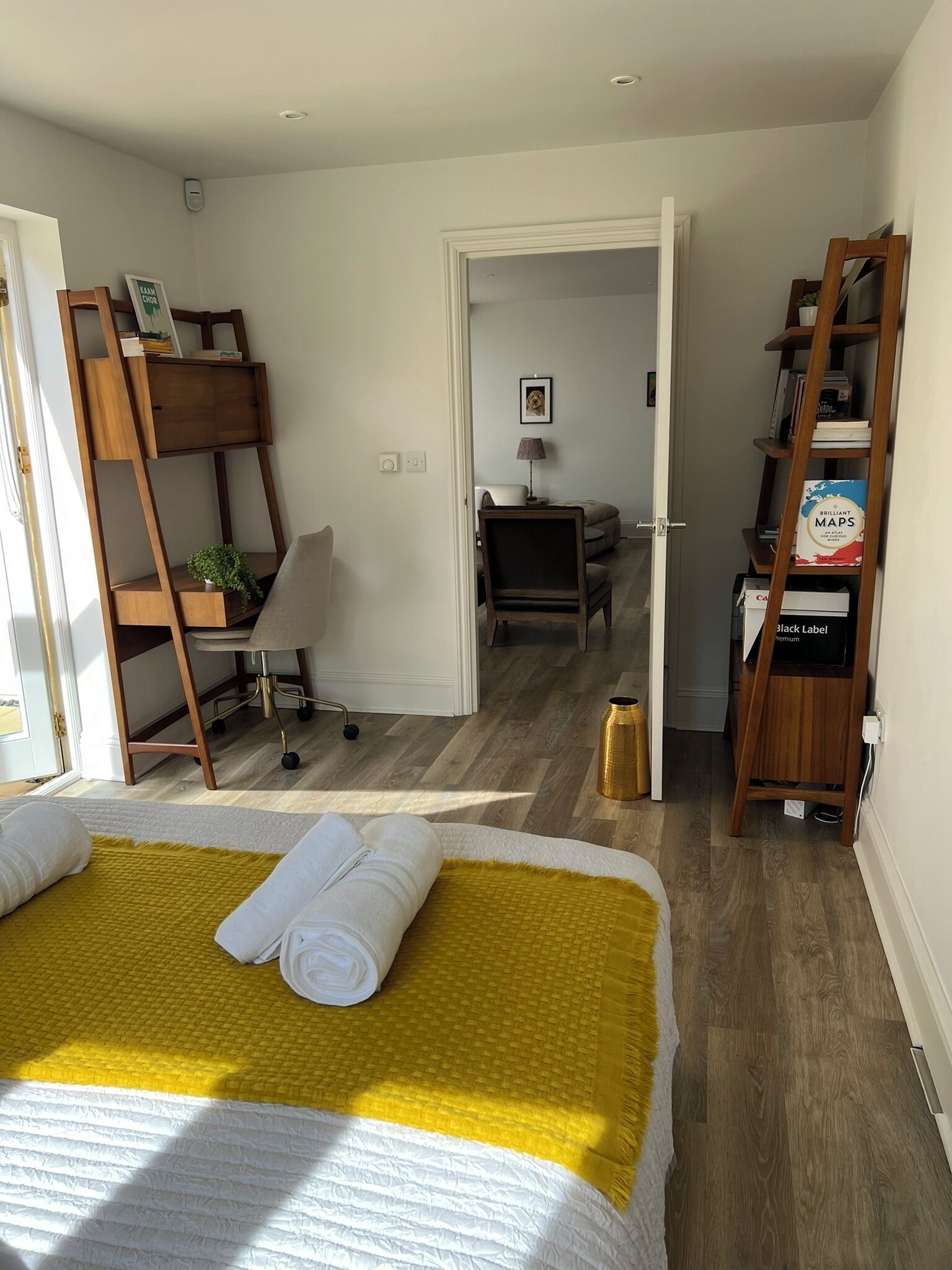 A bedroom with a bed, a desk, a chair, a bookshelf, and a door leading to another room.