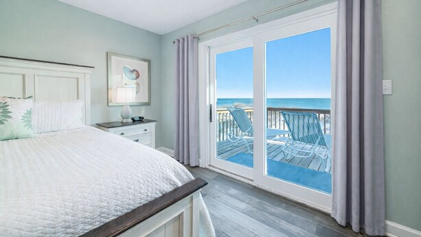 A bedroom with a bed, a nightstand, a framed picture, and a view of the beach through a sliding door. - BEACHFRONT, BEAUTIFUL, FULLY RENOVATED HOUSE! (Gulf Shores)