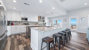 A spacious kitchen with white cabinets, a large island with bar stools, and a view to the outside. - BEACHFRONT, BEAUTIFUL, FULLY RENOVATED HOUSE! (Gulf Shores)