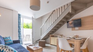 A modern living room with a sofa, coffee table, and a staircase leading to a dining area. - Résidence Odalys Collection Rève d'Ile by Interhome (Ile de Re)