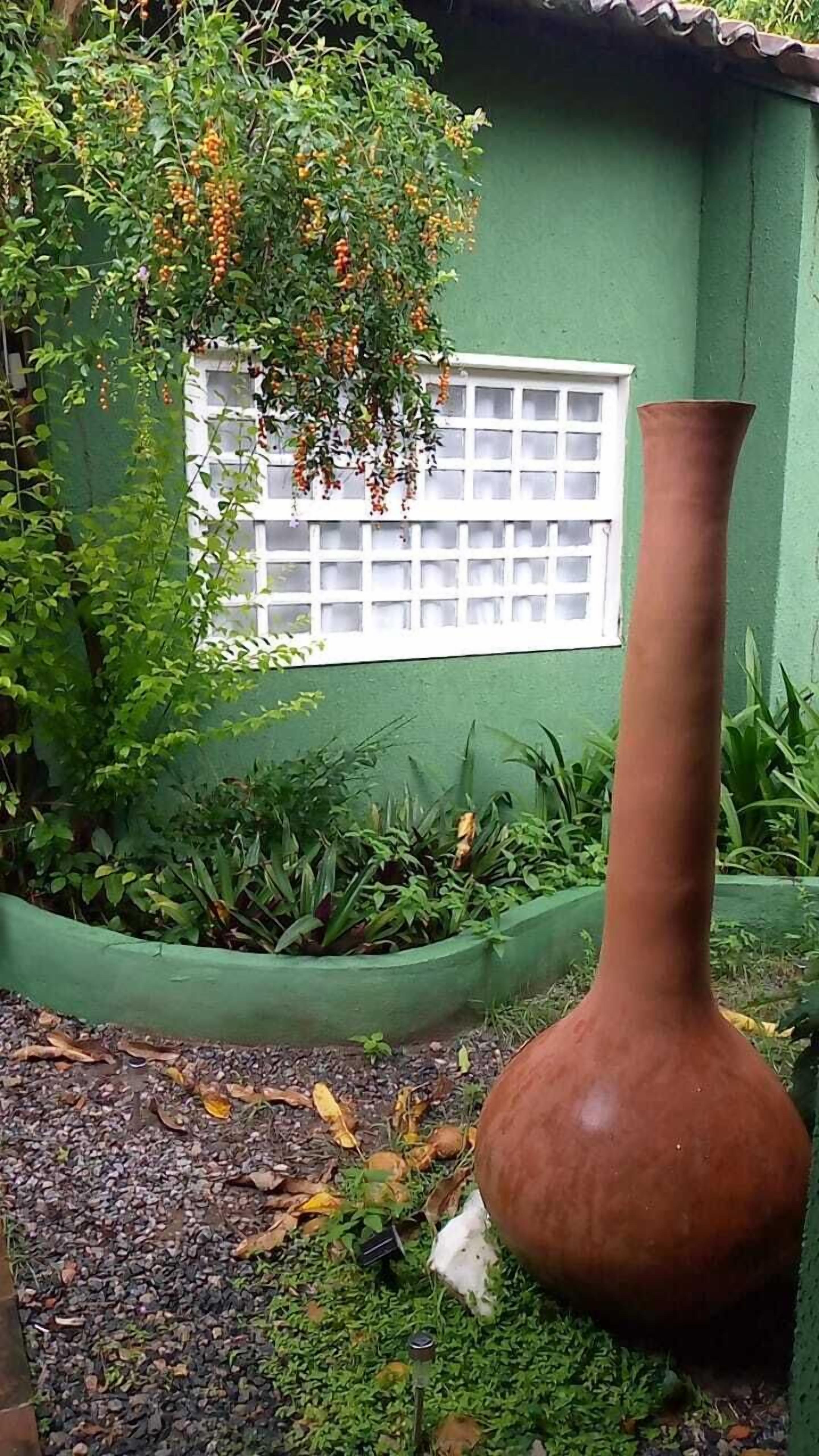 Un gerro de terracota gran en un jardí amb parets verdes i una finestra amb un disseny de reixa.
