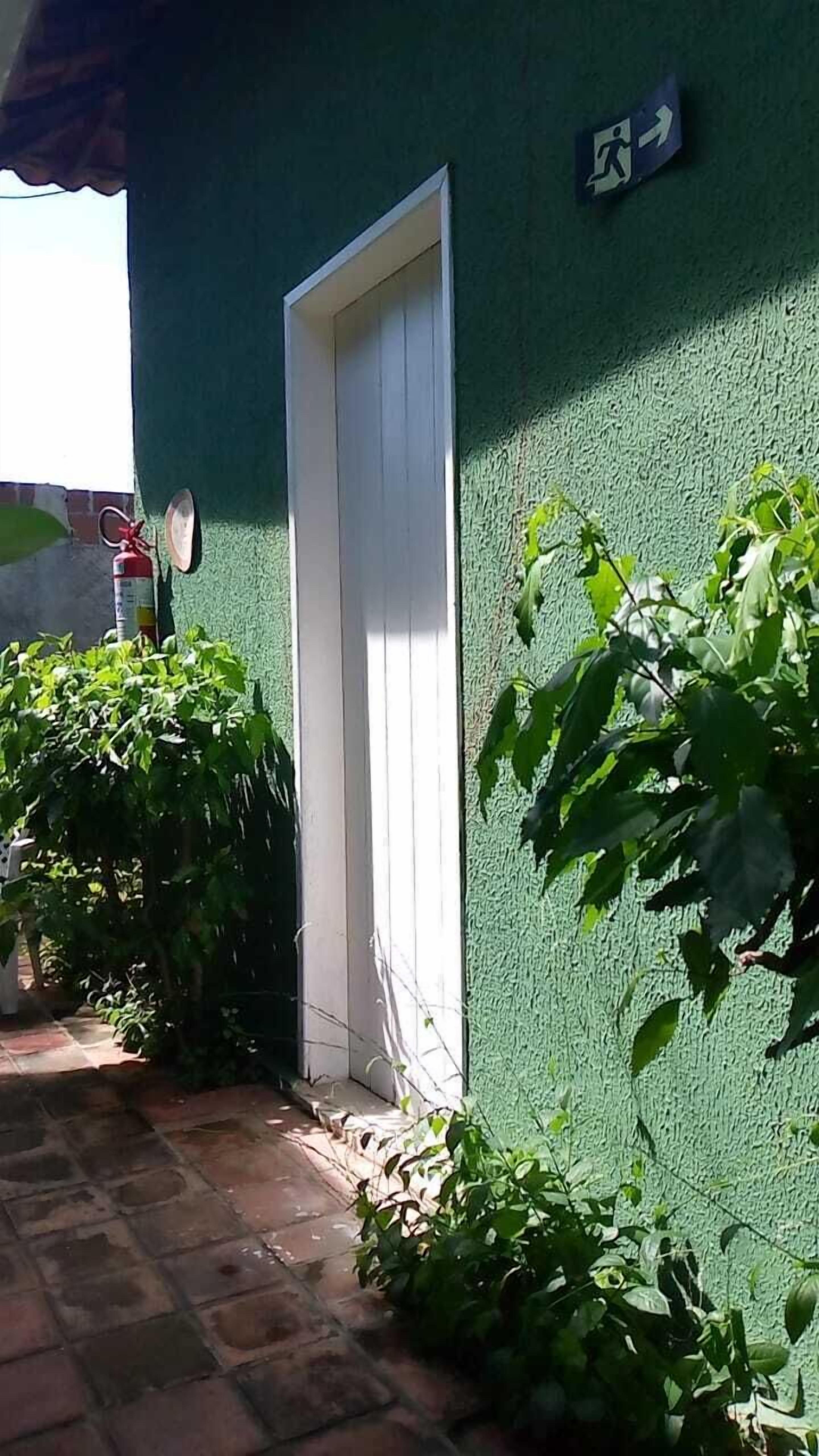 Una parete esterna verde con una porta bianca, un estintore e un cartello direzionale.