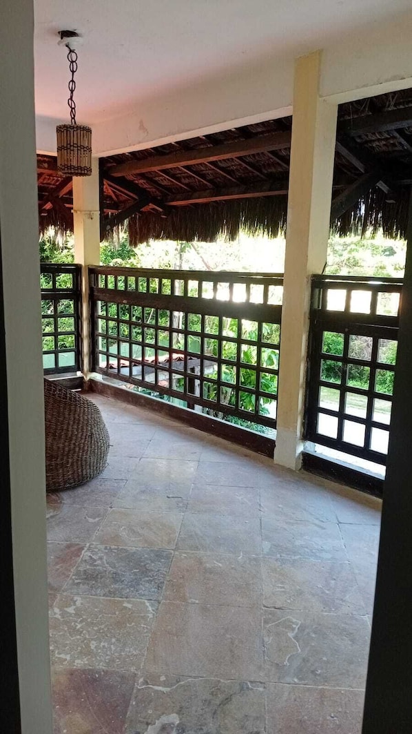 A covered outdoor area with stone flooring, a wicker seating area, and a metal railing.