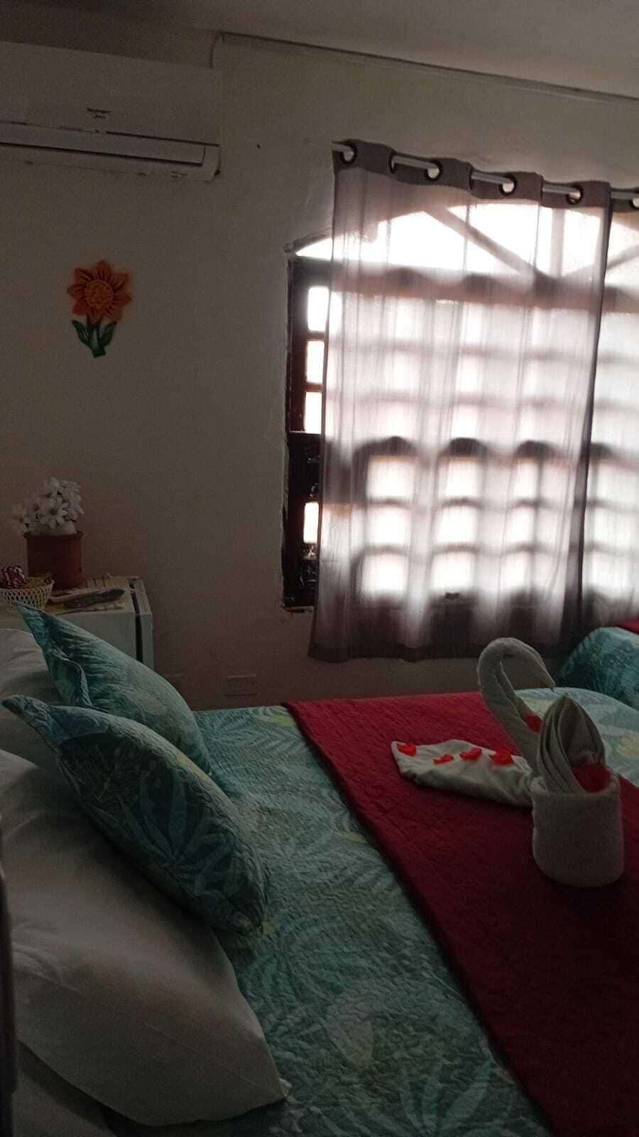 Ein Hotelzimmer mit Bett, Kissen, einer roten Decke, einem Handtuch und einem Fenster mit Vorhängen.