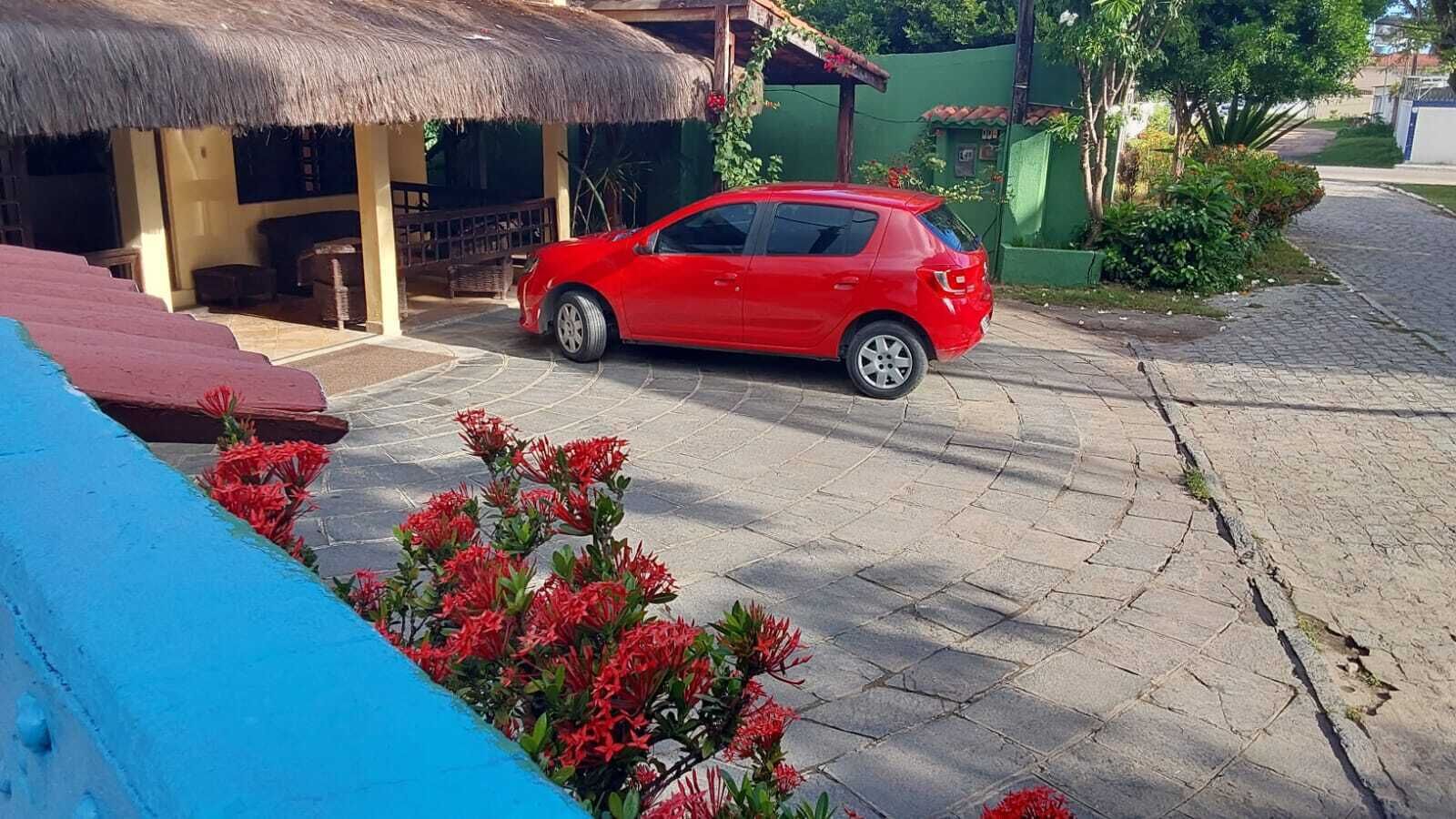 A red car parked in front of a building with a thatched roof.