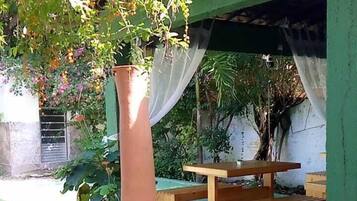 A large terracotta vase in a garden setting with a wooden table and chairs under a green structure.
