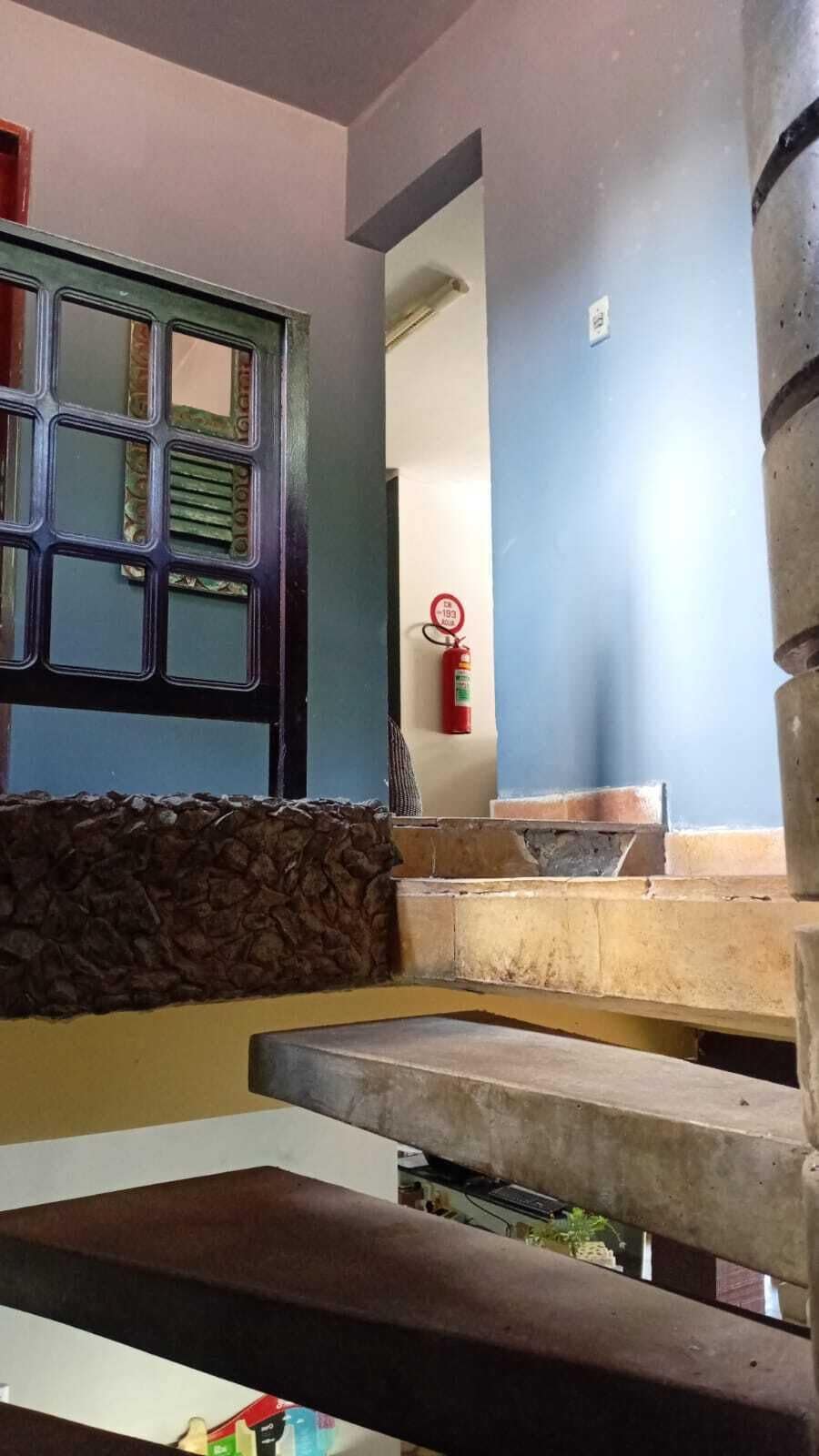 A staircase with stone steps, a fire extinguisher mounted on the wall, and a window with a metal grille.