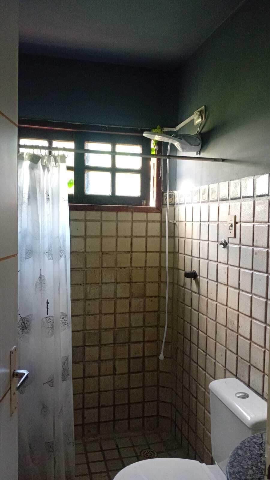 Un baño pequeño con azulejos, ducha, inodoro y ventana con cortina.