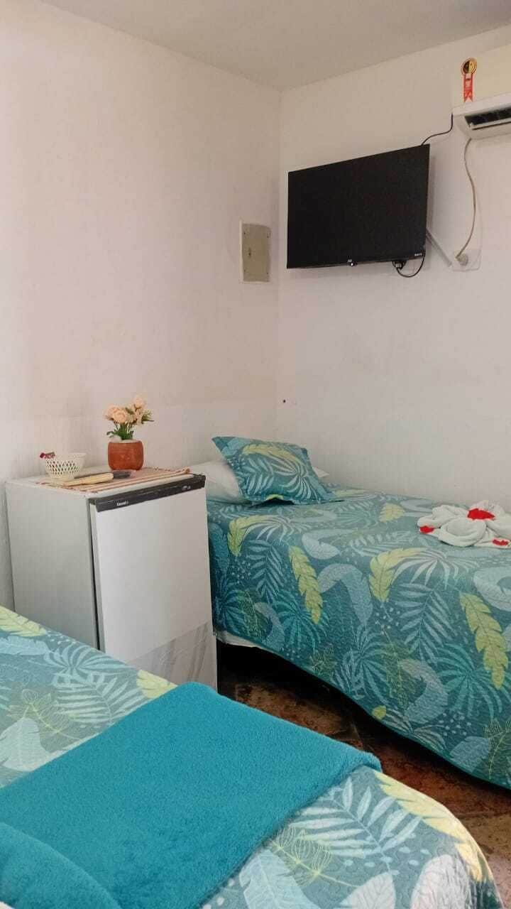 A room with two beds, a small table with a plant, a television mounted on the wall, and a wall-mounted air conditioning unit.