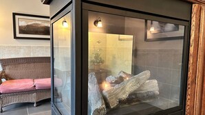 Une cheminée moderne avec un encadrement en verre, un canapé en osier et un tableau encadré accroché au mur.