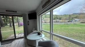 Une pièce moderne dotée d’une grande fenêtre, d’une petite table ronde, d’un fauteuil gris et d’un téléviseur à écran plat fixé au mur.