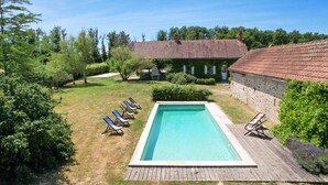 Ein rechteckiger Pool mit Holzterrasse, umgeben von einer Rasenfläche und Bäumen.