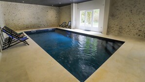 Una piscina interior con vista despejada al agua, un techo con iluminación empotrada y un ventanal que proporciona luz natural.