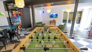 Una mesa de fútbol de mesa en una habitación con sofás verdes, un televisor y una decoración mural colorida.