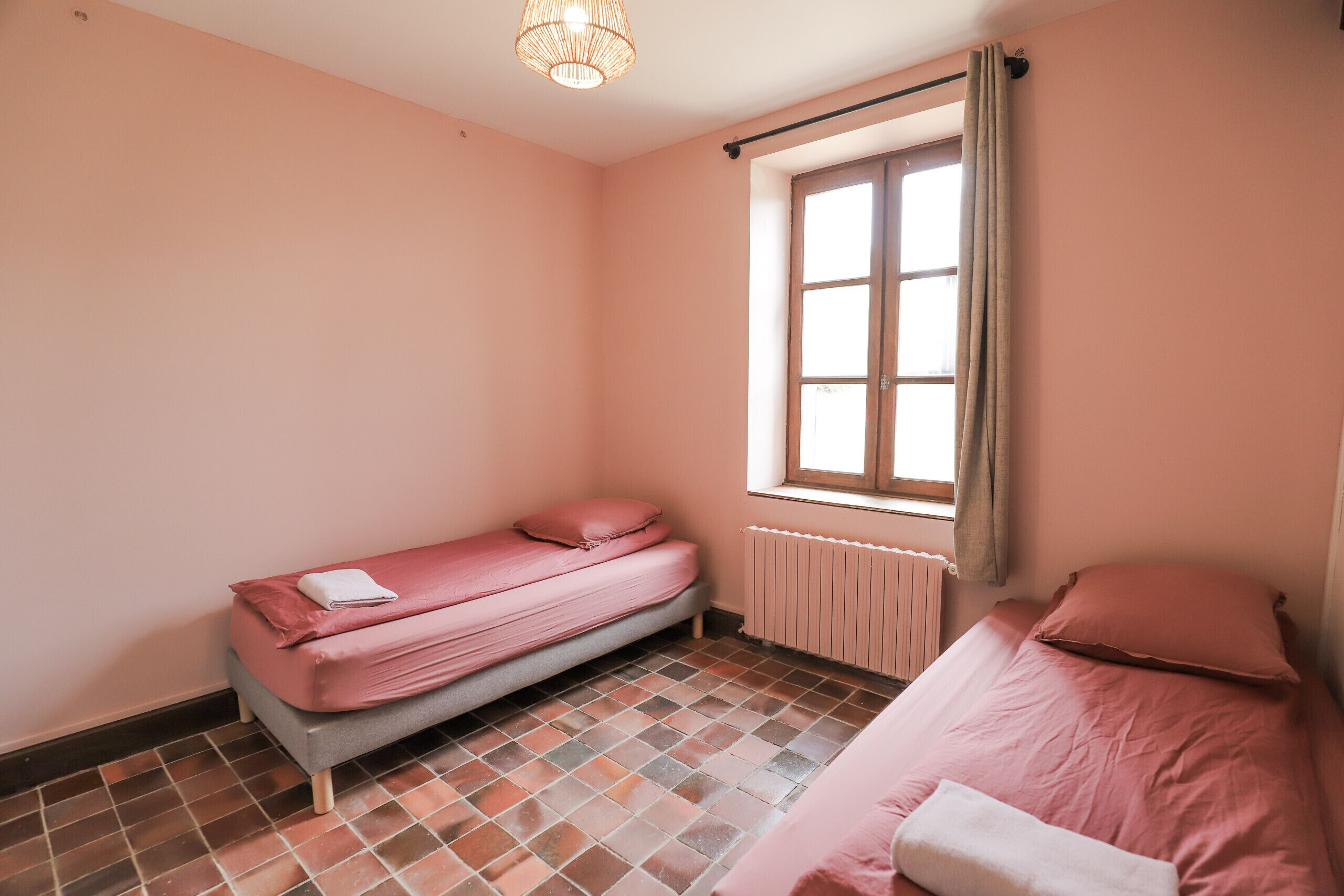 A small, pink-themed room with a single bed, a window with curtains, and a radiator.