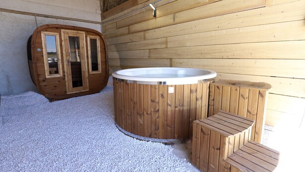 Une cabane en bois avec un jacuzzi, une porte en bois et un petit banc en bois.