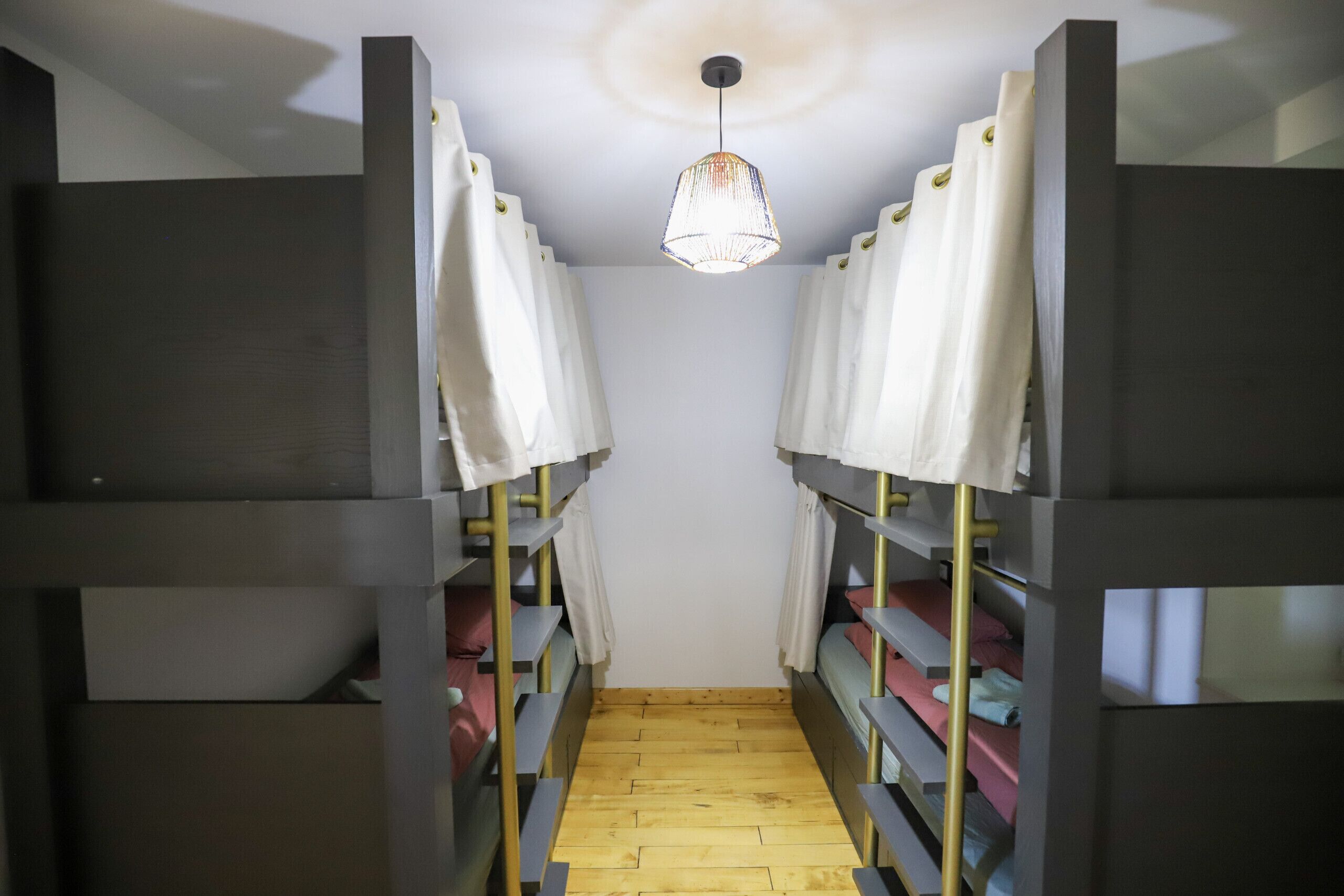 A narrow hallway with bunk beds on either side, a wooden floor, and a hanging light fixture.