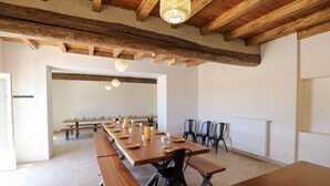 Un vaste espace dédié à la salle à manger, avec de longues tables en bois et des chaises noires, agrémenté de poutres apparentes et caractérisé par un design simple et épuré.