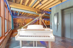 A grand piano in a spacious room with exposed wooden beams and a brick wall.