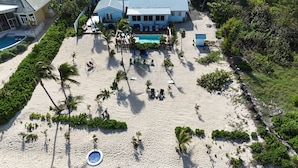 An aerial view of a beach resort with a swimming pool, lounge chairs, and palm trees. -  Cayman Bliss - Beachfront house private Pool & Beach Sleeps 8 Family-Friendly (West Bay)