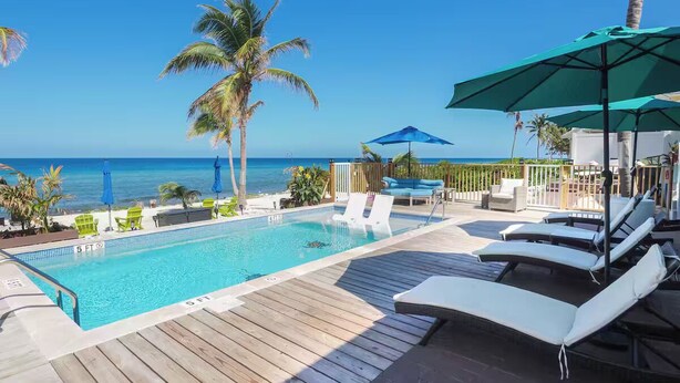 A poolside area with lounge chairs and umbrellas, overlooking the ocean. -  Cayman Bliss - Beachfront house private Pool & Beach Sleeps 8 Family-Friendly (West Bay)