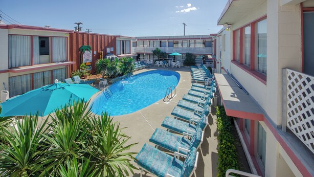Un espace piscine doté de chaises longues et de parasols, entouré d’immeubles avec des balcons.