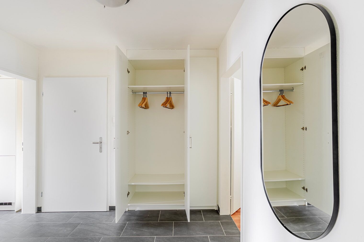 Un dressing avec les portes ouvertes, un miroir et des vêtements suspendus.