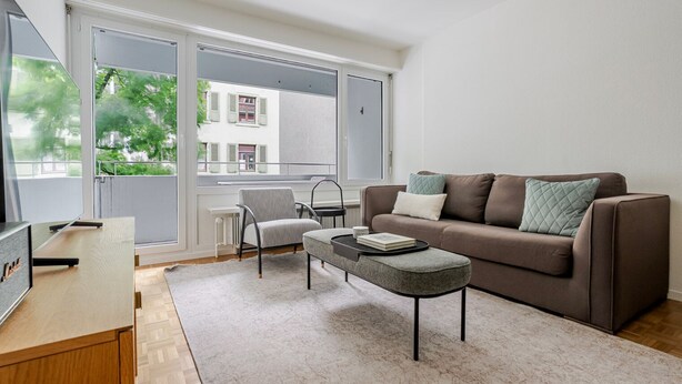 A modern living room with a sofa, armchair, coffee table, and a TV on a wooden stand. - Blueground | Basel-Matthäus, view, nr Kunstmuseum (Basel)