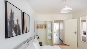 A modern bedroom with a bed, two framed artworks, a wardrobe, and a hallway leading to another room. - Blueground | Basel-Matthäus, view, nr Kunstmuseum (Basel)