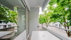 A balcony with a white table and chairs, a glass door, and a view of trees and buildings. - Blueground | Basel-Matthäus, view, nr Kunstmuseum (Basel)