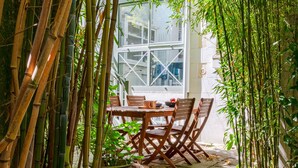Un jardin de bambous avec une table et des chaises, un pot de fleurs et une fenêtre donnant sur des bâtiments.