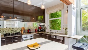 Une cuisine moderne avec des meubles de couleur sombre, un plan de travail blanc, un four encastré et une fenêtre donnant sur un paysage verdoyant.