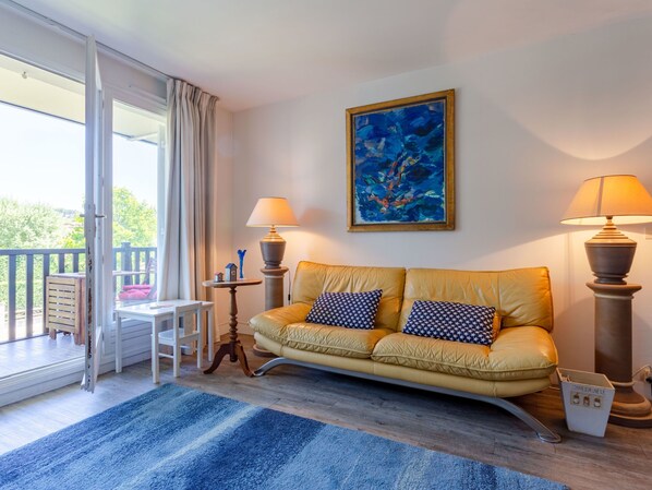A room with a sofa, two lamps, a painting, a small table, and a view through a glass door. - Eden Park by Interhome (Deauville-Trouville)