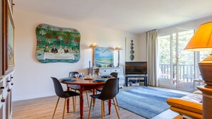 Ein Essbereich mit Holztisch und -stühlen, einem Gemälde an der Wand, einem Fernseher und einem Fenster mit Vorhängen.