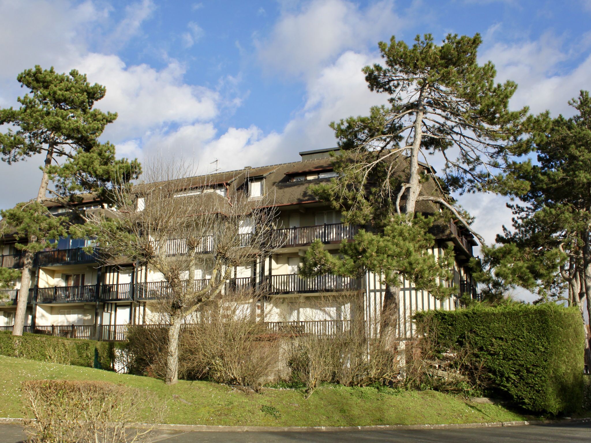 A multi-story building with balconies, surrounded by trees and a well-maintained lawn.