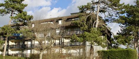 A multi-story building with balconies, surrounded by trees and a well-maintained lawn.