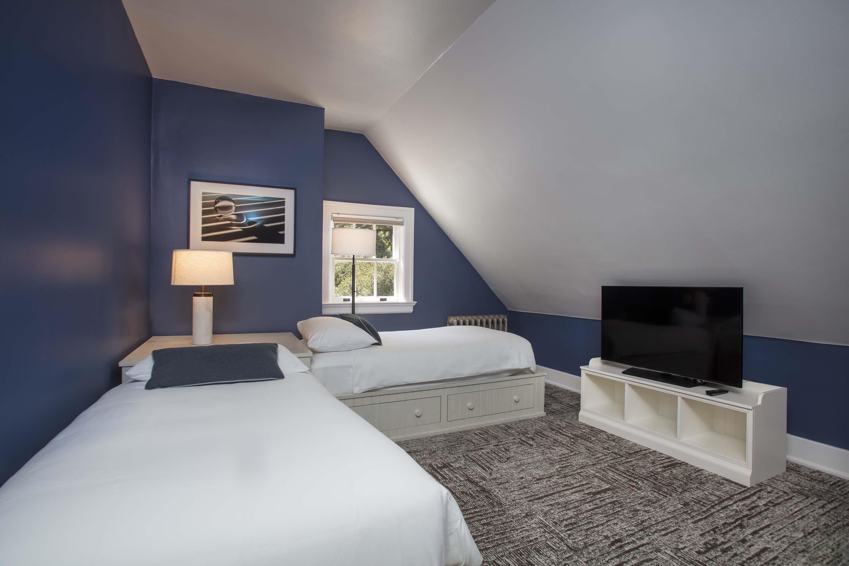 A bedroom with two beds, a TV on a stand, a window, and a picture on the wall.