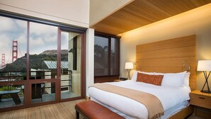 A hotel room with a large bed, wooden headboard, two bedside lamps, a bench, and a sliding glass door leading to an outdoor area with a view of the Golden Gate Bridge. - King Room at a 4.5⭐️ Hotel (Sausalito)
