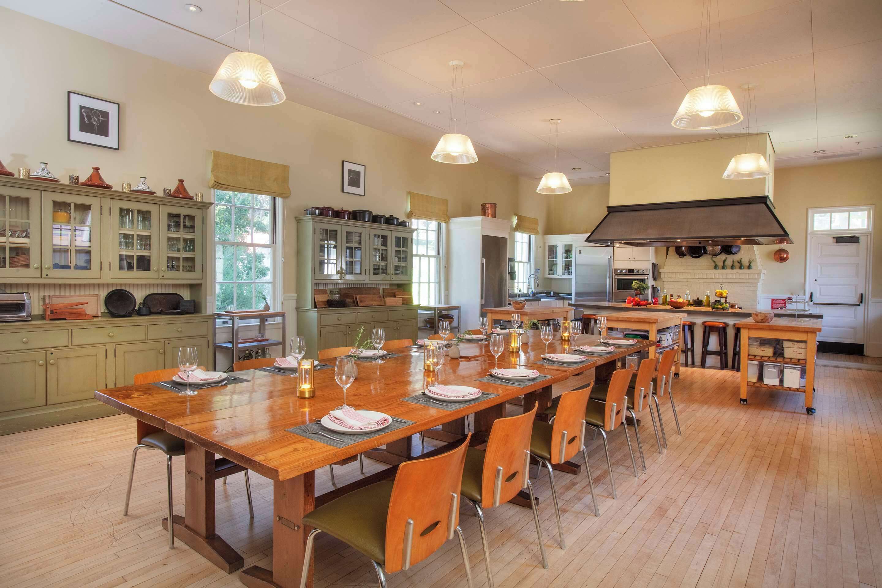 A spacious kitchen with a large wooden dining table set for six, surrounded by wooden chairs. There are multiple cabinets and a built-in oven.
