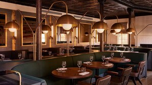 Un restaurant avec des tables rondes, des banquettes vertes et des luminaires suspendus en laiton.
