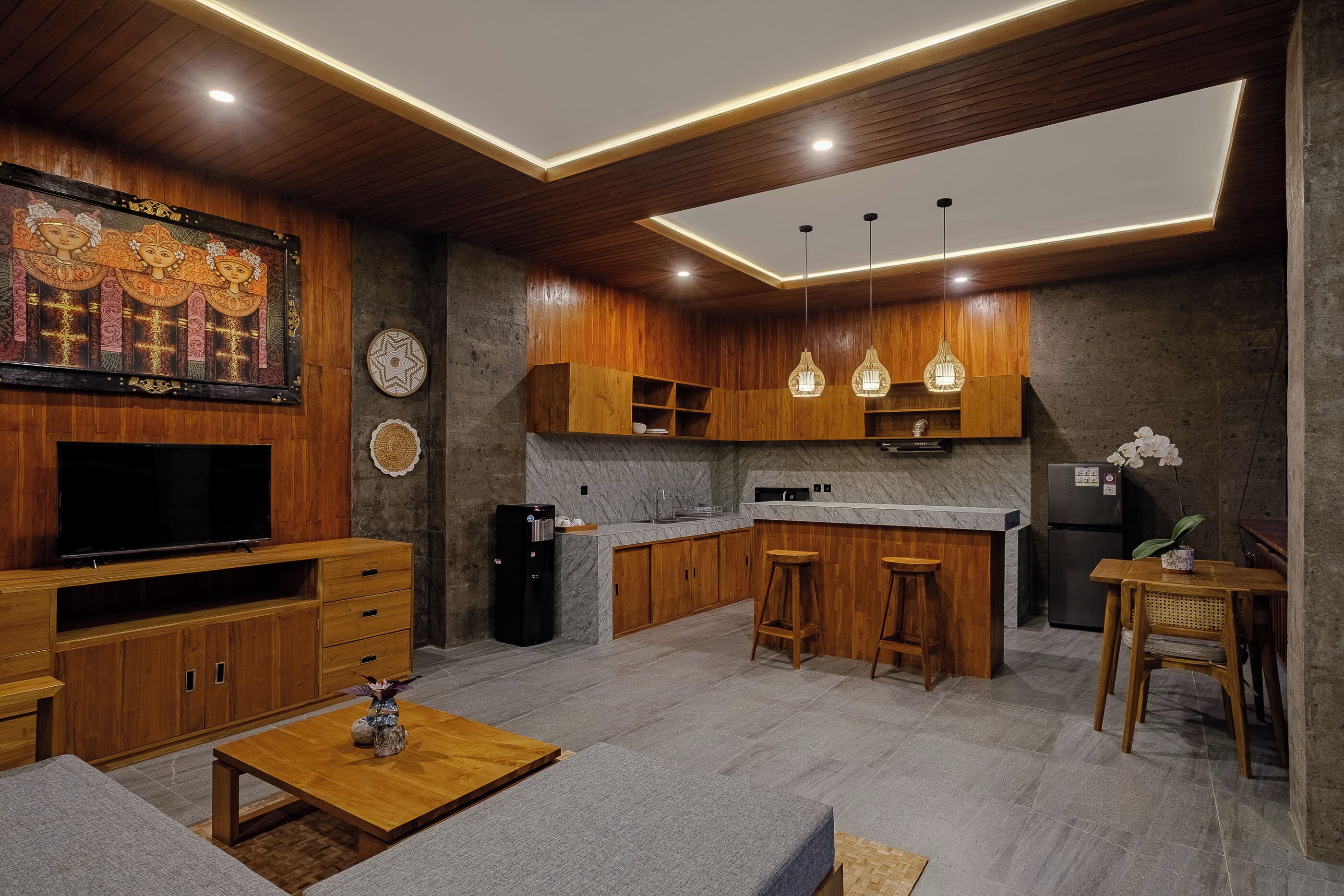 A modern kitchen with wooden cabinets, a marble countertop, and a built-in oven. There is a dining area with a wooden table and bar stools.