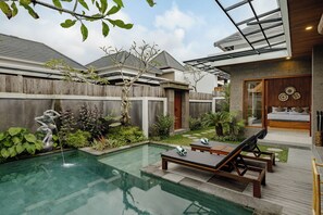 Un espace piscine extérieur moderne, doté de chaises longues, d’une terrasse en bois et d’un mur en pierre.