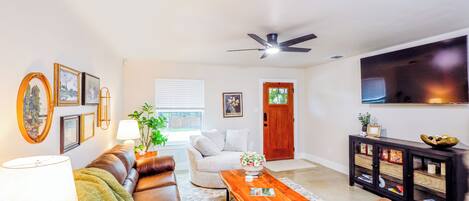 A living room with a brown leather sofa, a wooden coffee table, a white armchair, and a TV on the wall.