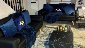 A modern living room with two black sofas, blue velvet cushions, and a marble coffee table. - 2-Bed - Sleeps 4 - Pet Friendly & Free Parking (Bolton)