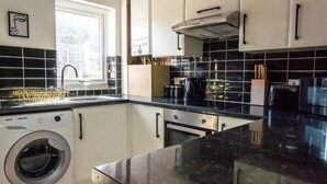 A compact kitchen with a washing machine, a stove, and a coffee maker. - 2-Bed - Sleeps 4 - Pet Friendly & Free Parking (Bolton)