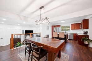 Une cuisine spacieuse avec des meubles en bois, un coin repas doté d’une grande table et de chaises, et un escalier menant à un autre niveau.