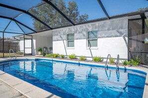 Una piscina con zona cubierta, un edificio blanco con ventanas y una cerca.